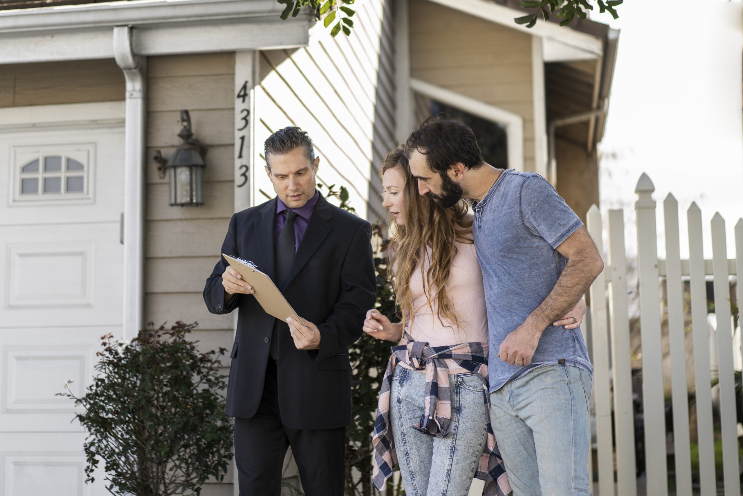 couple-signing-papers-fr-new-house A real estate agent showing a couple a piece of paper in front of a home
