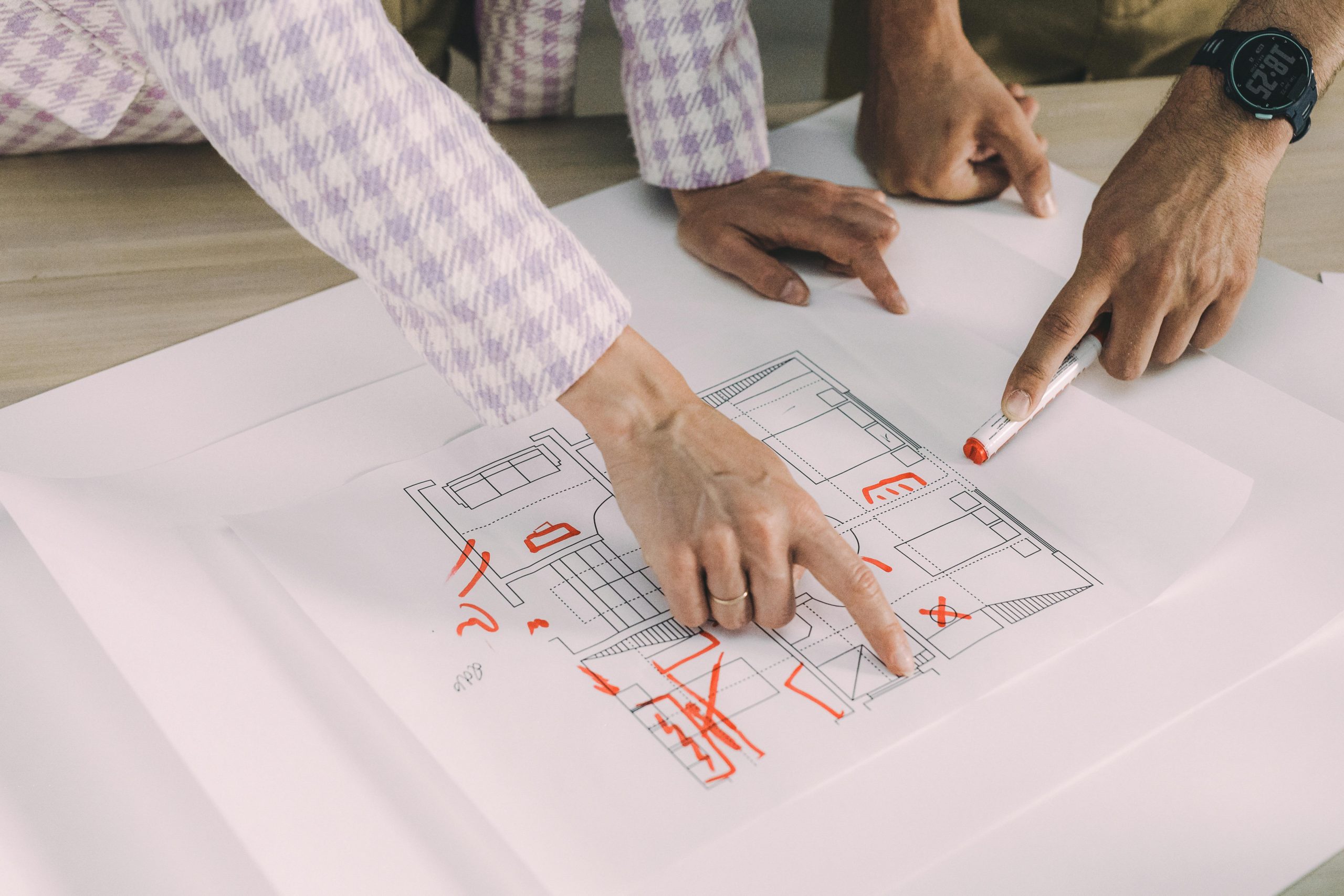 pexels-shvets-production-9052547 Two people discussing and pointing at construction blueprints. The blueprints are marked with a bright red marker